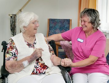 Die Pflegerin hält die Hand der Bewohnerin im Rollstuhl.